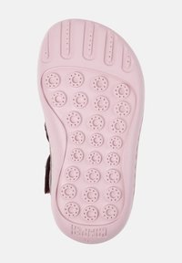 Semelle d'une sandale rose pour enfants avec des grips texturés circulaires et le nom de la marque "Camper" embouti près du talon.
