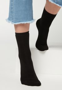 Calcetines negros de altura tobillo hechos de una tela suave, combinados con vaqueros cortos azules con dobladillos deshilachados. Diseño simple y sin costuras.