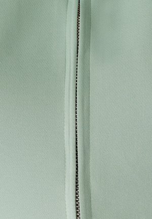 Miętowa tkanina z centralnym zamkiem błyskawicznym, z metalowymi ząbkami i gładką teksturą, otoczona złożonymi brzegami dla schludnego wykończenia.