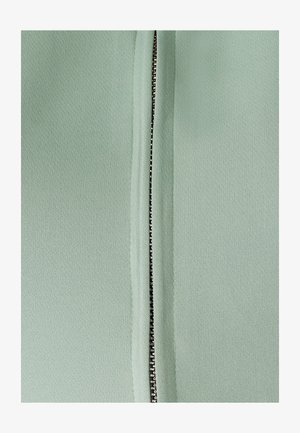 Miętowa tkanina z centralnym zamkiem błyskawicznym, z metalowymi ząbkami i gładką teksturą, otoczona złożonymi brzegami dla schludnego wykończenia.