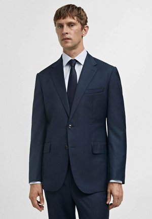Navy suit jacket with two buttons, notched lapels, and chest pocket. Tailored fit with smooth fabric and contrasting white shirt underneath.