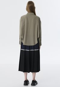 Losse olijfgroene blouse met lange mouwen en een afgeronde onderkant, gecombineerd met een geplooide zwarte en marineblauwe rok met een kanten accent.