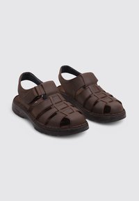 Las sandalias de cuero marrón presentan un diseño de punta abierta con correas trenzadas, hebilla ajustable y una suela de goma texturizada para agarre y comodidad.