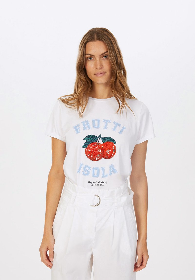 White cotton t-shirt featuring a red sequined cherry graphic with green leaves, and blue "FRUTTI ISOLA" lettering. Styled with high-waisted white pants.