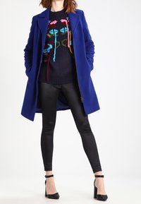 Tmavě modrý svetr s barevným květinovým vzorem, jasně modrý kabát, černé legíny a černé lodičky na podpatku s pásky kolem kotníků.