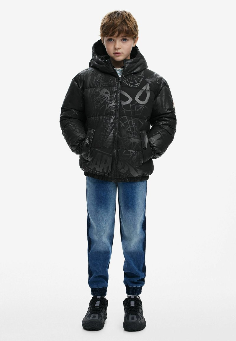Black puffer jacket with Spider-Man graphics, zip front, and hood. Dark blue jeans, elastic cuffs, and black sneakers complete the outfit.