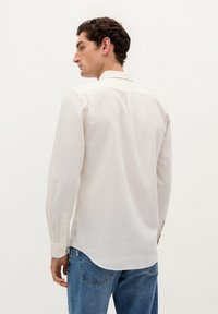 Lysstribet hvid skjorte med lange �ærmer, rundet kant og rygpanel, parret med blå denim jeans.
