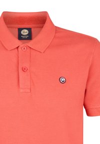 Koraalgekleurde polo met een gestructureerde stof, twee knopen bij de sluiting en een ronde logopatch in marineblauw op de linkerborst. Klassieke kraagontwerp.