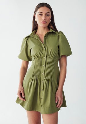 Oliviavihreä lyhythihainen mekko, jossa on nappilista ja poimutettu yläosa. Valmistettu pehmeästä kankaasta, flare-helma ja kaulus.