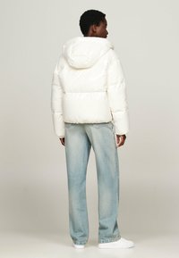 White puffer jacket with a hood, featuring quilted sections, elastic hem, paired with light blue jeans and white sneakers.