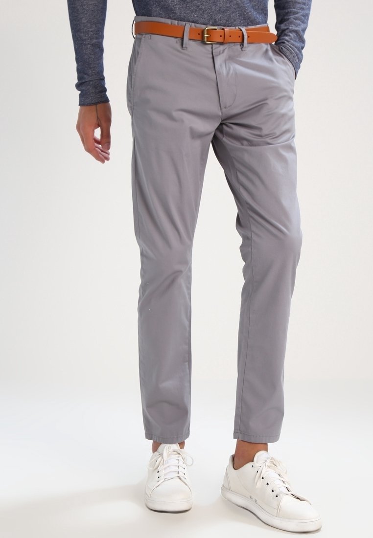 Grå, slim-fit byxor i ett mjukt tyg, med sidofickor och ett brunt läderbälte, kombinerat med vita sneakers.