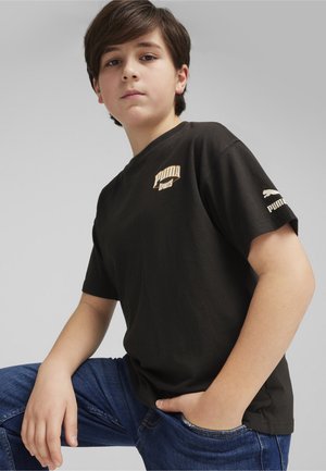 T-shirt di cotone nero con logo "Puma Sports" crema sul petto e logo Puma bianco sulla manica. Indossato con jeans blu.