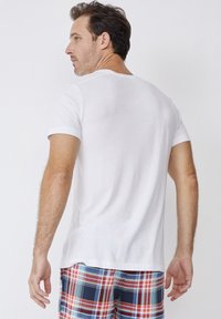 White cotton T-shirt with short sleeves, round neckline, plain design, worn with plaid shorts featuring red, blue, and green patterns.