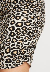 Leopardmönstrad tyg med svarta och beige fläckar på en vit bakgrund. Materialet är rynkat, vilket visar en volangdesign i nederkant.