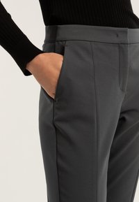 Szare spodnie o dopasowanym kroju, charakteryzujące się gładką fakturą, z bocznymi kieszeniami i płaskim przodem. Noszone z dopasowanym czarnym swetrem z prążkowanej dzianiny.