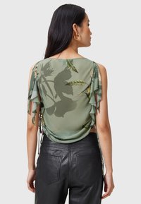 Top in seta verde con motivo floreale, maniche arricciate e schiena drappeggiata. Abbinato a pantaloni in pelle nera aderenti.