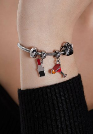 Zilveren armband met bedeltjes in de vorm van een lipstick, een cocktailglas en een handtas. De armband heeft een flexibele vormgeving met een gladde textuur.