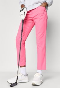 Rozā golfa bikses ar šauru piegriezumu, izgatavotas no gludas auduma. Savai izskatam pievienotas baltas sporta kurpes un golfa nūja, ar kontrastējošu cimdu.