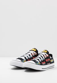Schwarze Leinensneaker mit Batman-Grafiken in Rot, Gelb und Blau, weißen Schnürsenkeln und Gummisohlen. Flaches Design, im Low-Top-Stil.