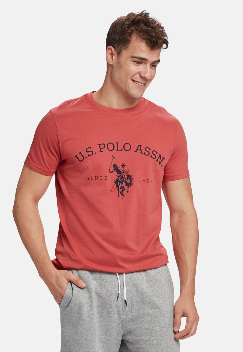 Crvena pamučna majica s okruglim izrezom, s mornarskoplavim grafičkim prikazom igrača polo i natpisom "U.S. POLO ASSN. SINCE 1890" jasno istaknutim.