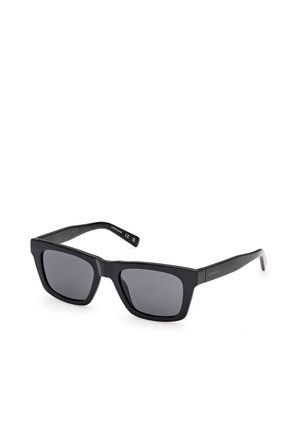 Schwarze rechteckige Sonnenbrille mit dicken Rahmen und dunkel getönten Gläsern, leicht schräg auf weißem Hintergrund dargestellt.