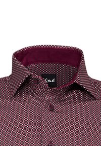 Camicia a righe rosse e bianche con colletto alla francese, dotata di bottoni rotondi e un colletto interno di un profondo color mogano. Tessuto testurizzato con un design geometrico.