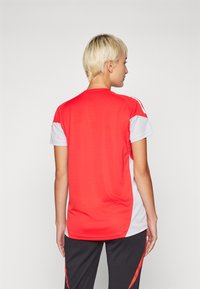 Rød og hvit sportstrøye med korte ermer, rund hals, glatt tekstur og kontrasterende sidepaneler.