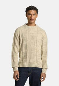 Beige stickad tröja med strukturerad mönster, rund halsringning och ribbade ärmslut och nederkant. Bärs tillsammans med mörkblå jeans.