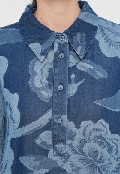 Cămașă din denim cu guler, plachetă cu nasturi și model floral în nuanțe variate de albastru. Textură netedă cu accente contrastante de un albastru mai deschis.