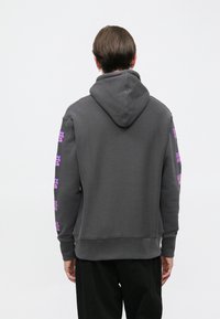 Grauer Kapuzenpullover aus strukturiertem Stoff, mit lebhaften pinkfarbenen Grafikmustern entlang beider Ärmel und einer Kängurutasche vorne.