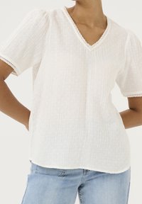 Camiseta blanca de manga corta con escote en V, fabricada con tela texturizada y con delicado borde de encaje en el cuello y las mangas. Corte informal, forma ligeramente holgada.