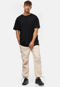 Sort t-shirt med korte ærmer og afslappet pasform, parret med lysebeige elastiske bukser med manchetter og sorte sneakers. Enkelt design, blød tekstur.