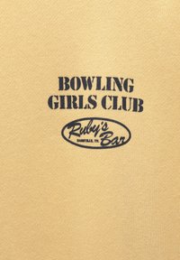 Tissu beige avec texte noir en pochoir indiquant "BOWLING GIRLS CLUB" au-dessus de "Ruby’s Bar Nashville TN" à l'intérieur d'un contour ovale.