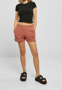 Černé vystřižené tričko, světle růžové sportovní šortky s elastickým pasem a bočními kapsami a černé pantofle na klopu s dvojitými popruhy.