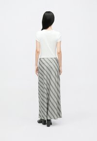 Maxinederdel i grå med diagonale striber, kombineret med en hvid tætsiddende top. Outfittet har en glat tekstur, ankellængde og blokhæle.