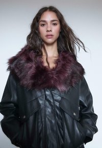 Sort læderjakke med en burgunderrød faux fur-krave, afslappet pasform, forlommer og metallisk trykknapslukning.