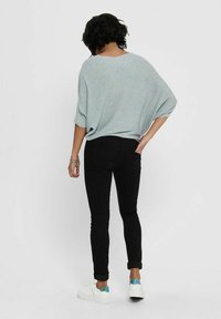 Jasnoniebieski teksturowany, oversize sweter w połączeniu z czarnymi obcisłymi dżinsami i białymi trampkami z kolorowym akcentem na pięcie.