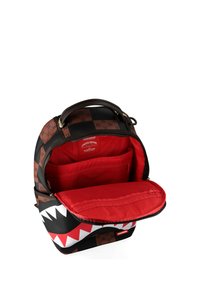 Mochila con patrón de cuadros en negro y marrón, diseño de boca de tiburón en el bolsillo frontal, y forro interior rojo con múltiples compartimentos.