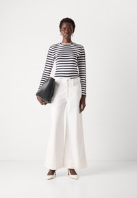 Camicia a righe a maniche lunghe in blu navy e bianco, abbinata a pantaloni bianchi a gamba larga e a una pochette nera. Tacchi bianchi a punta completano l'outfit.