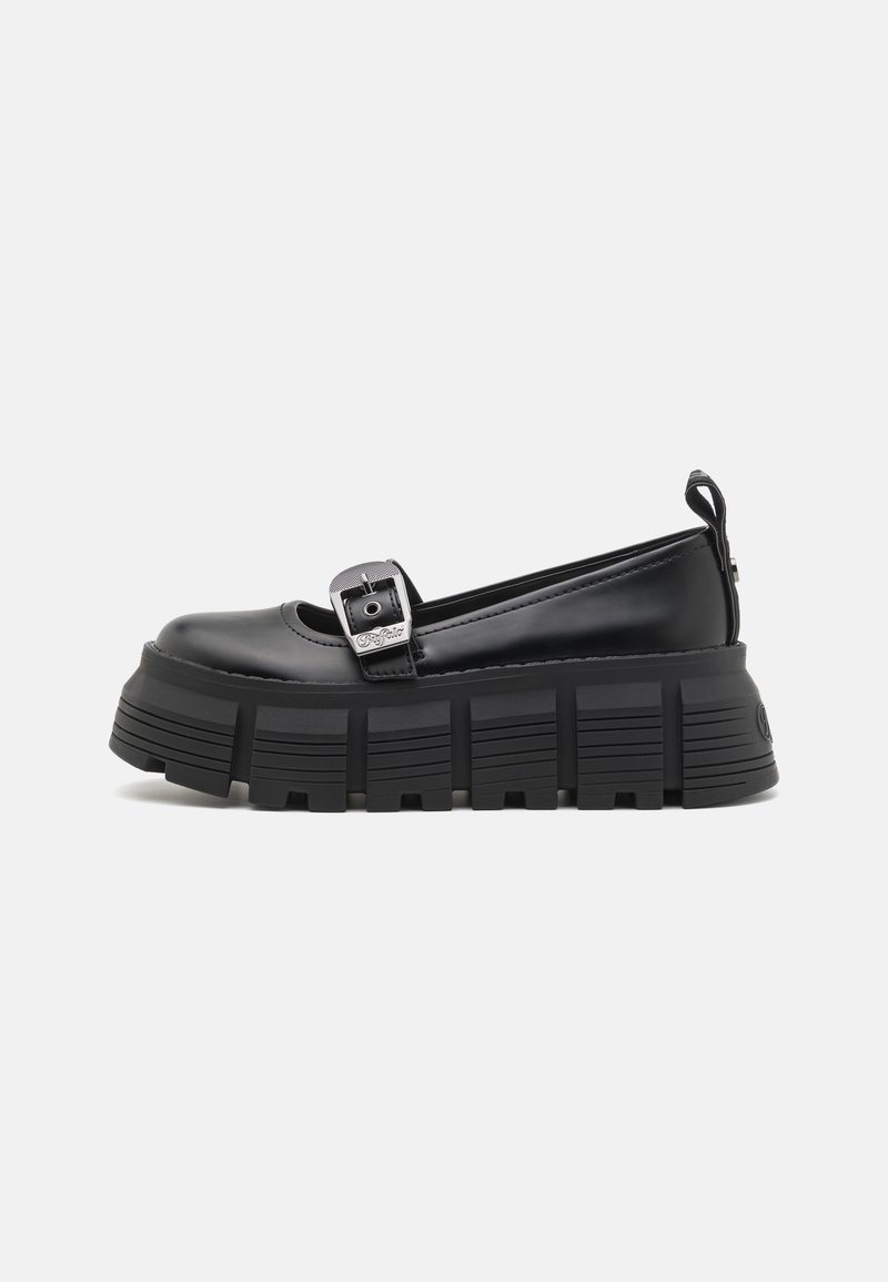 Chaussure Mary Jane noire avec semelle épaisse à rainures, bride avec boucle argentée et languette à l’arrière, vue de profil sur fond blanc.