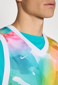 V-hals sports tank med et fargerikt akvarellmønster i nyanser av blått, rosa og grønt, med hvite detaljer og en liten Nike-logo.