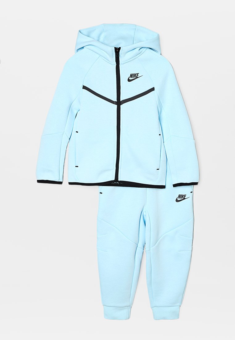 Ensemble en sweat à capuche zippé bleu clair et pantalon assorti, fabriqué en tissu doux ; comporte des accents noirs et un petit logo sur la poitrine et le pantalon.