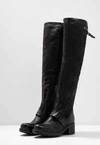 Botas altas de cuero negro hasta la rodilla con un diseño recto, cremallera lateral y un leve tacón. Material texturizado con un acabado suave y herrajes decorativos.