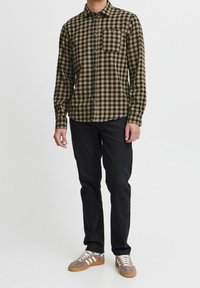 Černá a hnědá kostkovaná flanelová košile s dlouhými rukávy, límcem na knoflíky, s jednou náprsní kapsou, nošená s černými kalhotami a šedými teniskami.