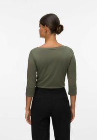 Olivgrünes Langarmshirt mit Bootsausschnitt, aus glattem Stoff und figurbetonter Silhouette, kombiniert mit hoch taillierten schwarzen Hosen.