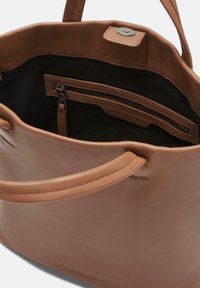 Torebka skórzana w kolorze tan, o gładkiej teksturze, z wnętrzem ze znaczkiem zamkiem oraz czarną podszewką. Posiada solidne uchwyty oraz magnetyczne zapięcie na zatrzask.