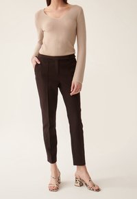 Pull beige à manches longues avec décolleté en V, associé à un pantalon droit marron foncé ajusté avec des plis marqués. Talons en cuir de serpent.