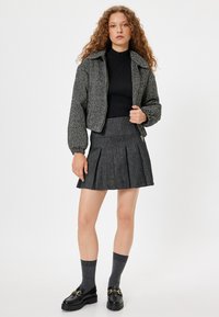 Svart och grå tweed kort jacka, ribbade svarta turtlenecks, vikta grå kjol, grå knästrumpor, svarta loafers med guldaccenter.