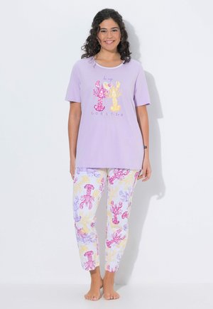 Vrouw draagt een lavendelkleurig shirt met korte mouwen met twee kreeften en bijpassende pyjamabroek met kreeftenprint, staat op blote voeten en lacht.