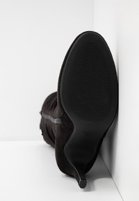 Botín de ante negro con puntera afilada, silueta elegante y suela texturizada. Cuenta con un tacón delgado y un sutil detalle de cremallera lateral.